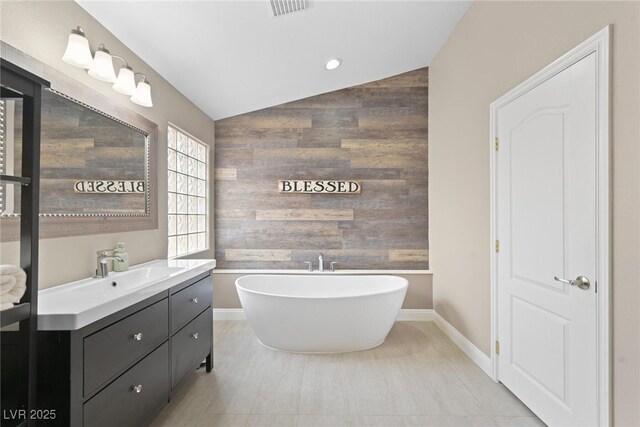 bathroom featuring vanity, lofted ceiling, a freestanding tub, wood walls, and an accent wall