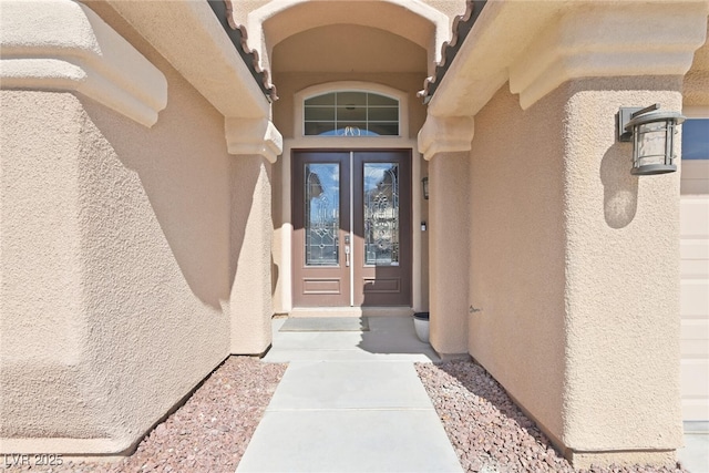 doorway to property with an attached garage, french doors, and stucco siding