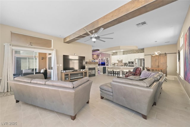 living area featuring a ceiling fan, visible vents, beam ceiling, a fireplace, and a barn door