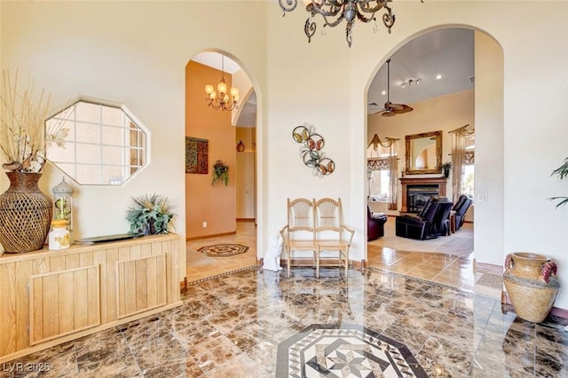 living area with arched walkways, ceiling fan, a glass covered fireplace, and a towering ceiling