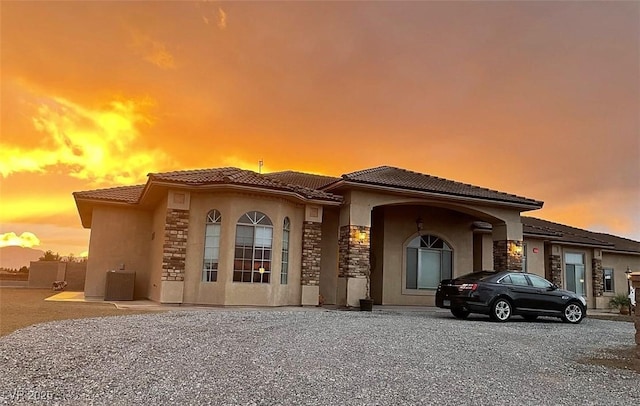 view of front of home with stone siding, a tiled roof, central air condition unit, and stucco siding