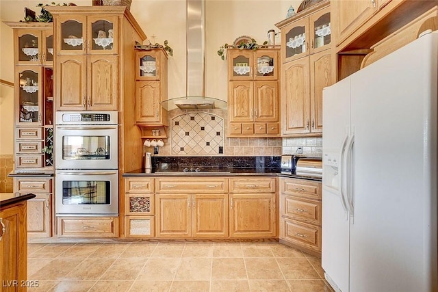 kitchen featuring white refrigerator with ice dispenser, dark countertops, backsplash, double oven, and wall chimney exhaust hood