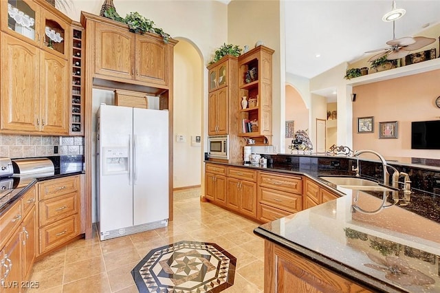 kitchen featuring light tile patterned floors, arched walkways, stainless steel microwave, white fridge with ice dispenser, and a sink