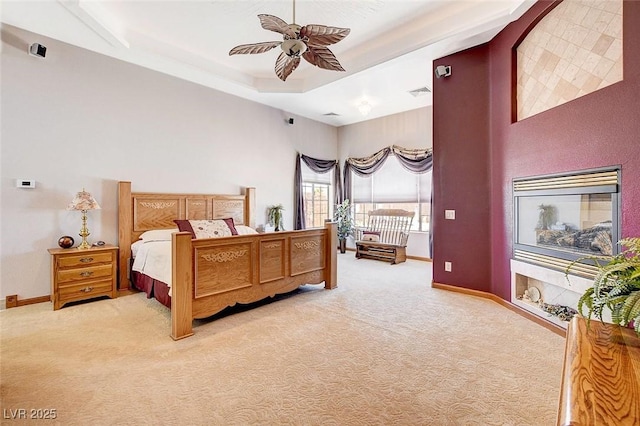 bedroom with a tray ceiling, visible vents, a ceiling fan, light carpet, and baseboards