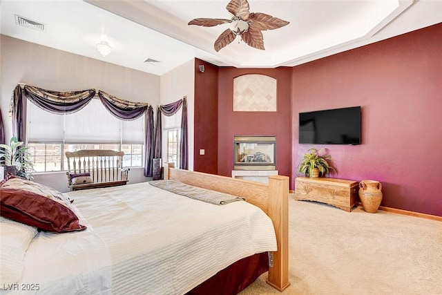 carpeted bedroom with ceiling fan, visible vents, a raised ceiling, and baseboards