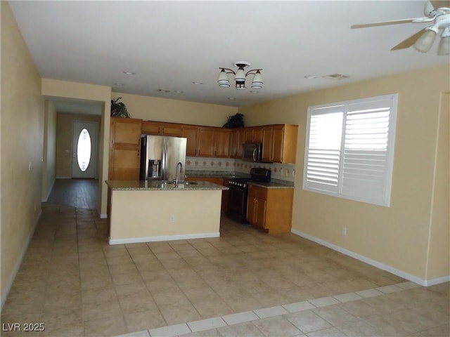 kitchen with a center island with sink, stainless steel appliances, backsplash, brown cabinetry, and a sink