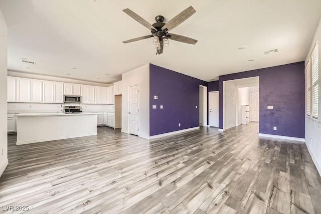 unfurnished living room with light wood finished floors, baseboards, visible vents, a ceiling fan, and a sink