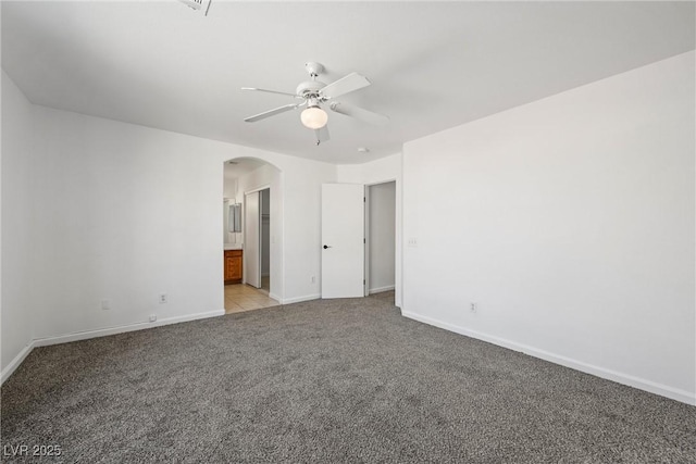 unfurnished bedroom with arched walkways, light carpet, connected bathroom, ceiling fan, and baseboards