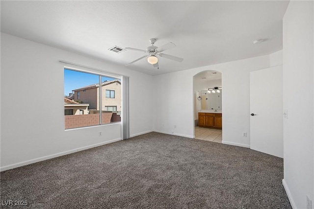 carpeted spare room featuring arched walkways, visible vents, ceiling fan, and baseboards