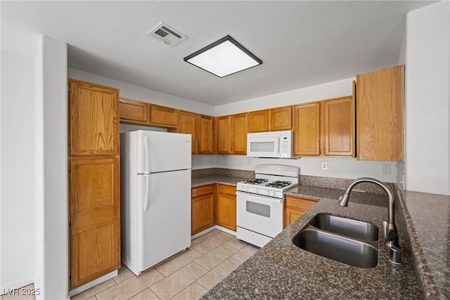 kitchen with white appliances, a sink, visible vents, brown cabinets, and dark stone counters