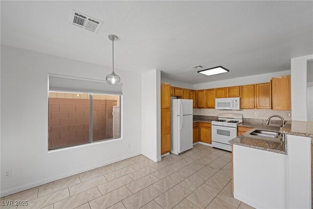 kitchen featuring white appliances, a sink, visible vents, brown cabinets, and dark stone counters