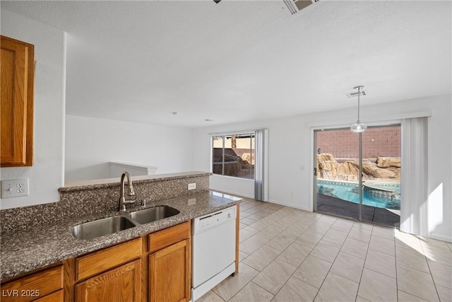 kitchen with visible vents, brown cabinetry, white dishwasher, a sink, and dark stone counters