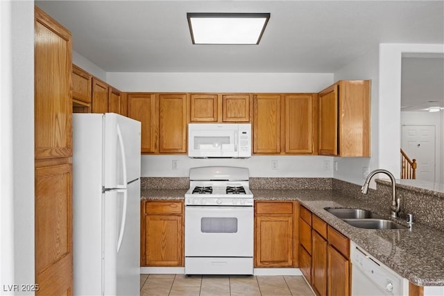 kitchen featuring brown cabinets, white appliances, dark stone counters, and a sink