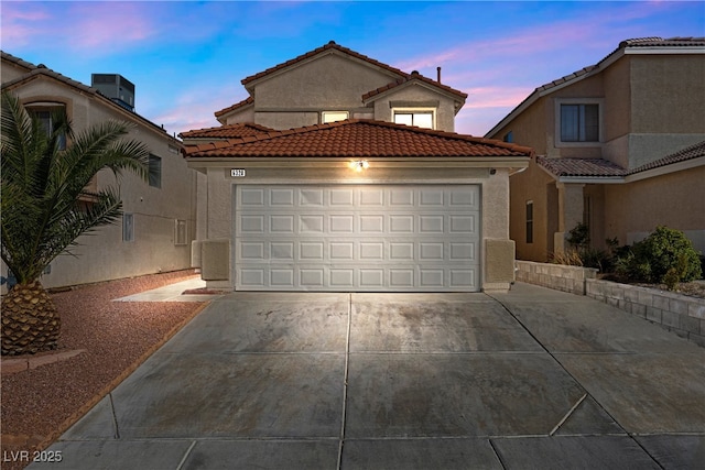 mediterranean / spanish house featuring concrete driveway, a tile roof, an attached garage, central AC, and stucco siding