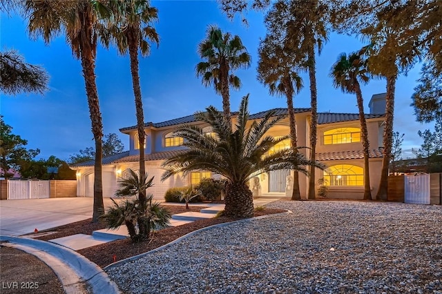 mediterranean / spanish house with a gate, fence, concrete driveway, and stucco siding