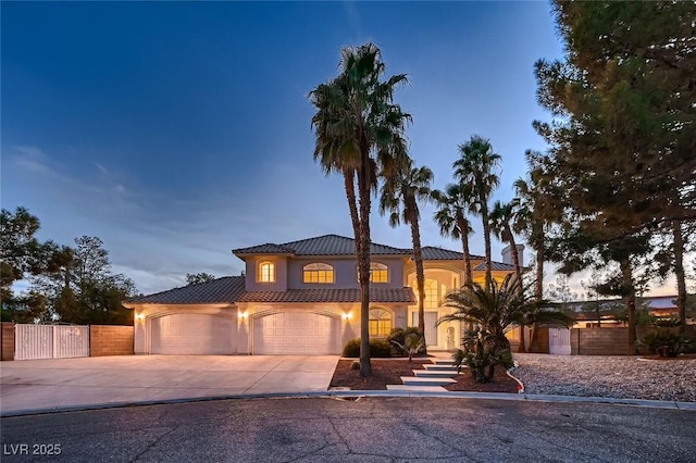 mediterranean / spanish home with stucco siding, an attached garage, a gate, fence, and driveway