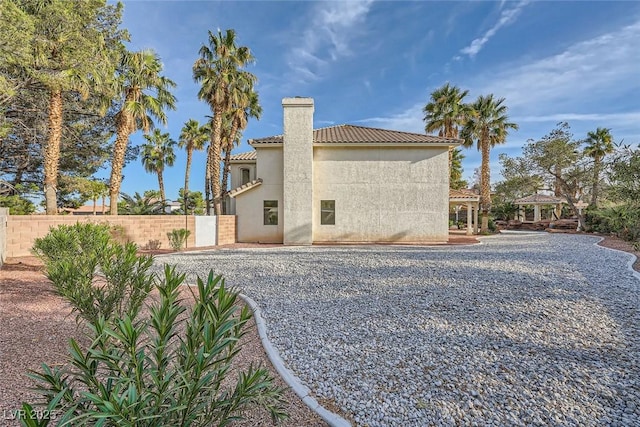 rear view of house with a tile roof, a chimney, stucco siding, a gazebo, and fence