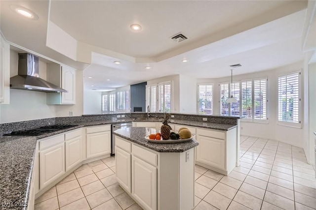 kitchen featuring a sink, visible vents, wall chimney range hood, stainless steel dishwasher, and black stovetop