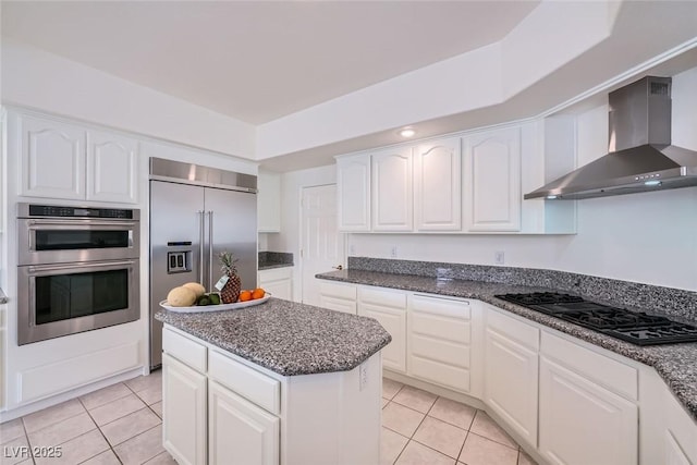 kitchen featuring light tile patterned floors, wall chimney exhaust hood, appliances with stainless steel finishes, and white cabinets