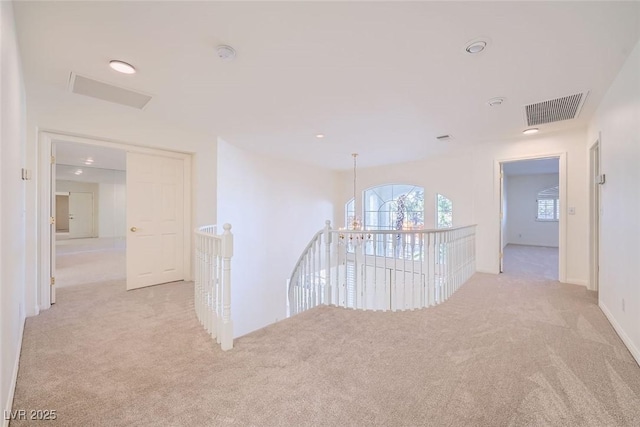 hall with an upstairs landing, visible vents, and light colored carpet