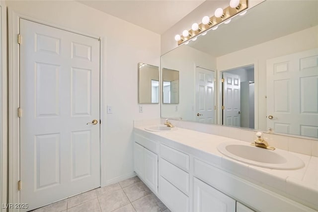 full bath featuring baseboards, double vanity, a sink, and tile patterned floors