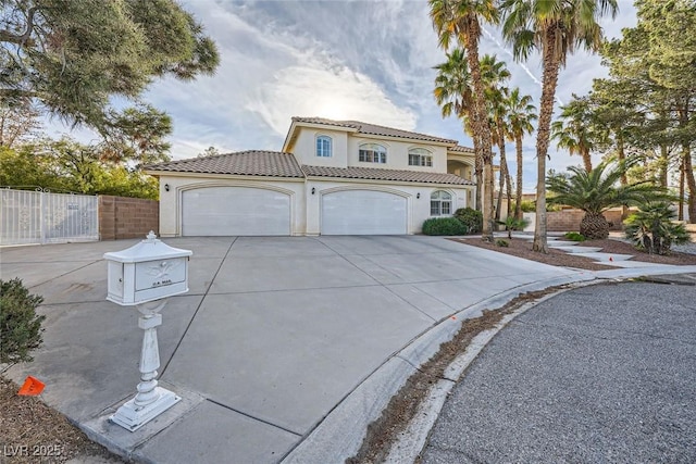 mediterranean / spanish house with an attached garage, fence, concrete driveway, a tiled roof, and stucco siding