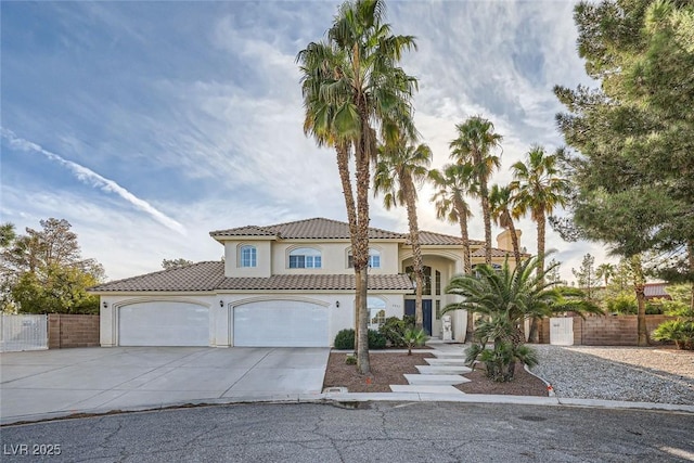 mediterranean / spanish home with a tile roof, stucco siding, concrete driveway, fence, and a garage