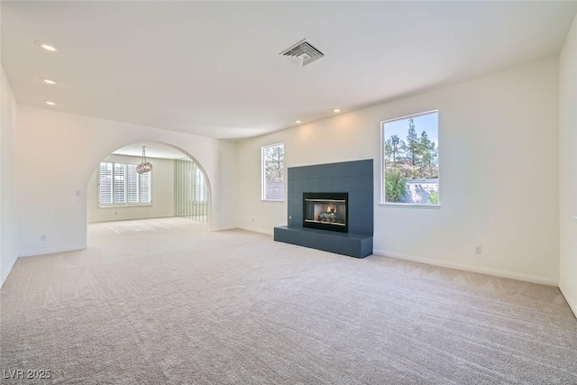 unfurnished living room featuring light carpet, arched walkways, a tile fireplace, and visible vents