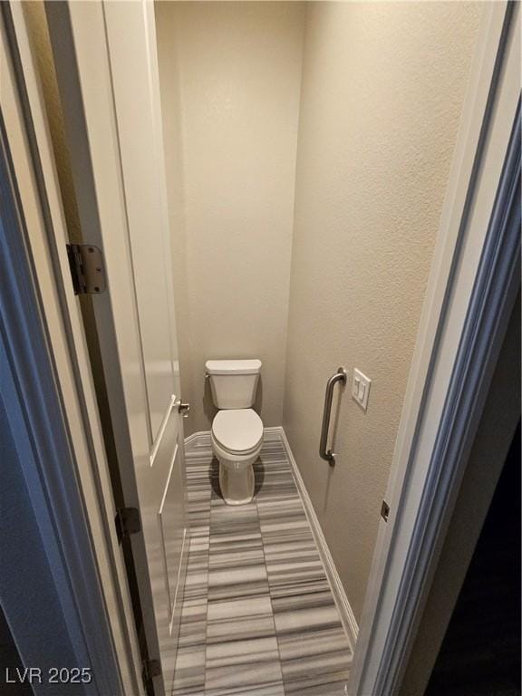 bathroom with toilet, baseboards, and a textured wall