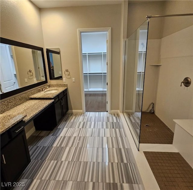 full bath with a walk in shower, a walk in closet, vanity, and baseboards