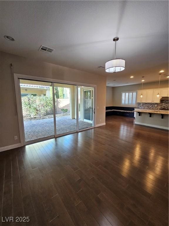 unfurnished living room featuring baseboards, visible vents, dark wood finished floors, and a wealth of natural light