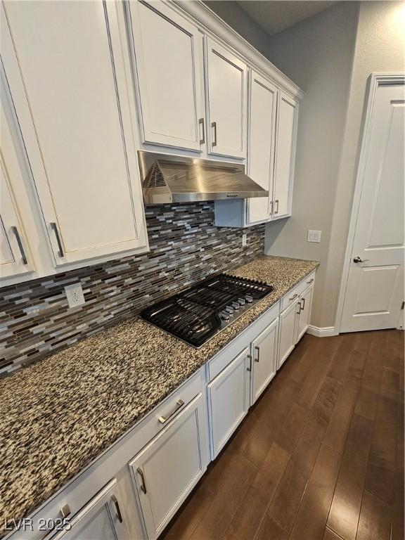 kitchen featuring decorative backsplash, dark stone counters, dark wood-style floors, under cabinet range hood, and stainless steel gas cooktop