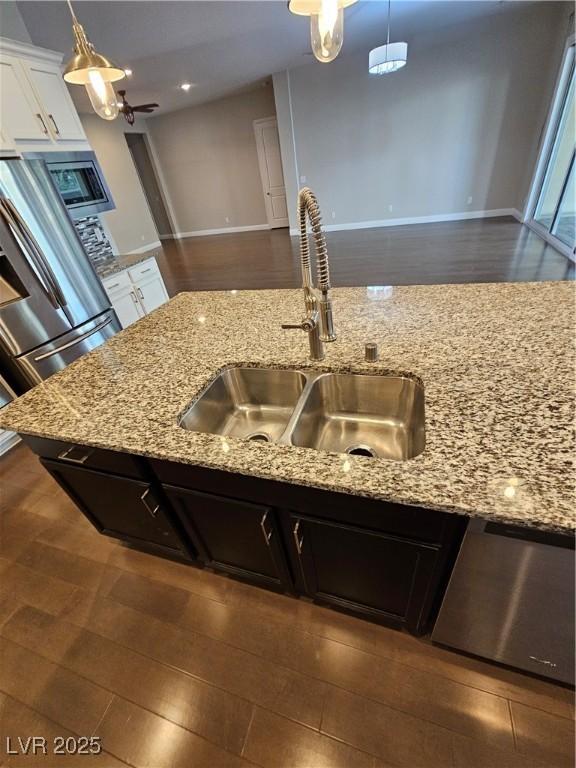 kitchen featuring appliances with stainless steel finishes, light stone counters, a sink, and decorative light fixtures