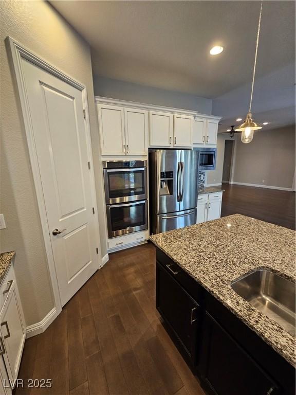 kitchen with white cabinets, light stone counters, stainless steel appliances, and dark wood-type flooring