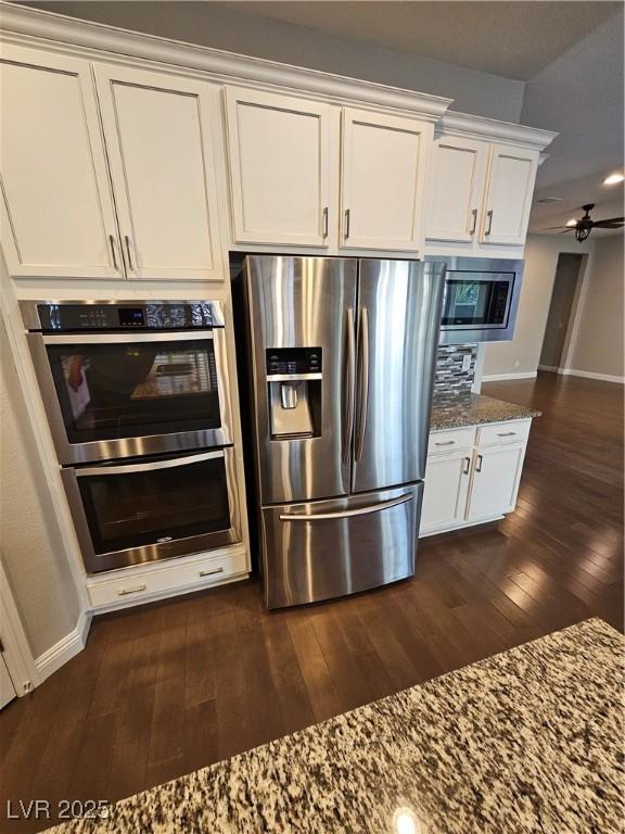 kitchen with white cabinetry, appliances with stainless steel finishes, dark stone counters, and dark wood finished floors