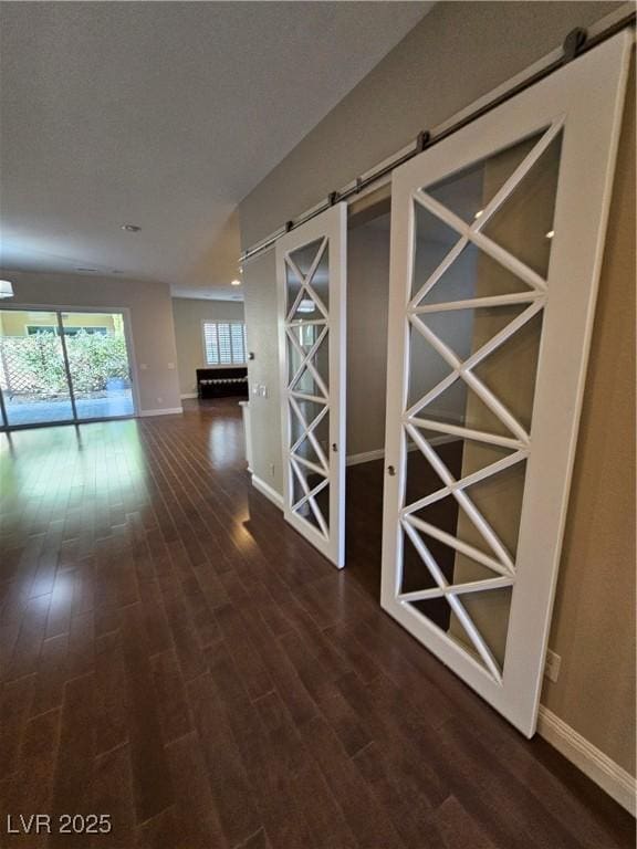 corridor with a barn door, dark wood-style flooring, and baseboards