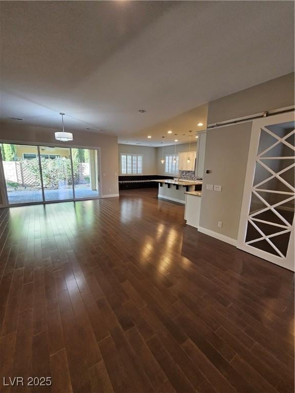 unfurnished living room with dark wood-style floors, a barn door, recessed lighting, and baseboards