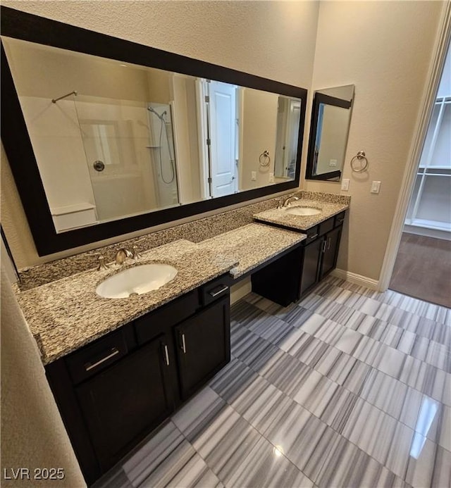 full bathroom featuring double vanity, baseboards, a shower, and a sink