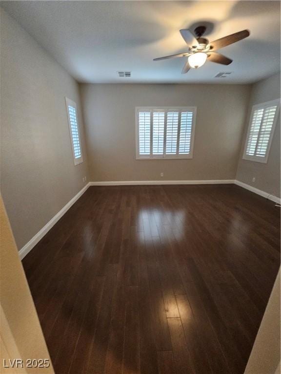 empty room with dark wood-style floors, visible vents, ceiling fan, and baseboards