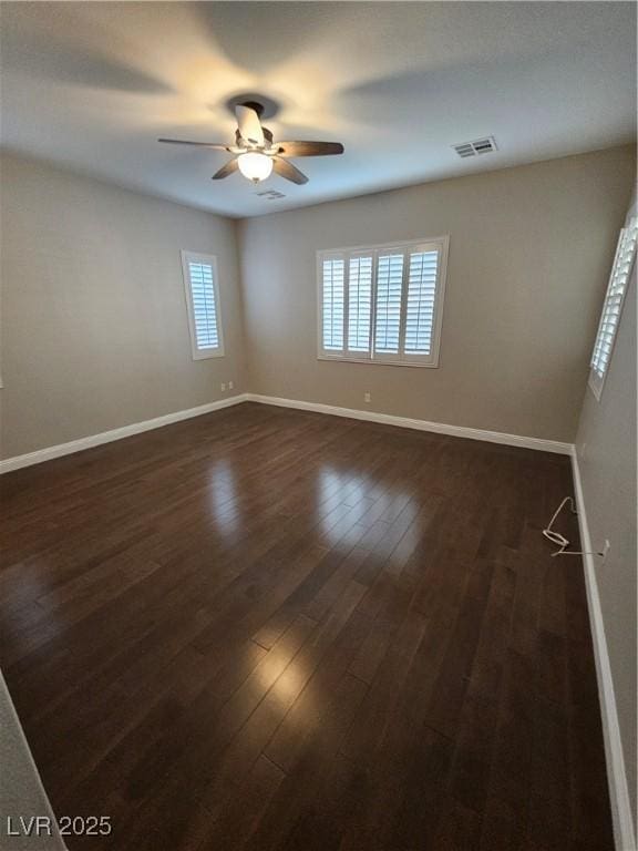 empty room with dark wood-style floors, baseboards, visible vents, and ceiling fan