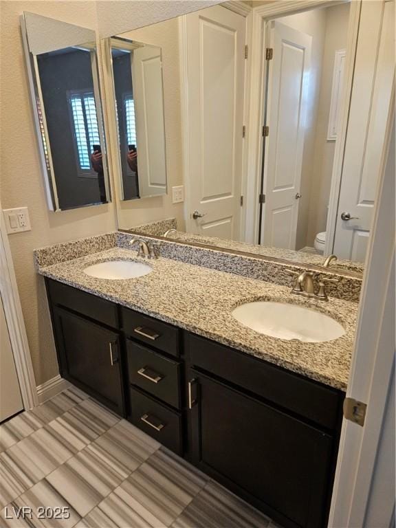 full bath with double vanity, a sink, toilet, and baseboards