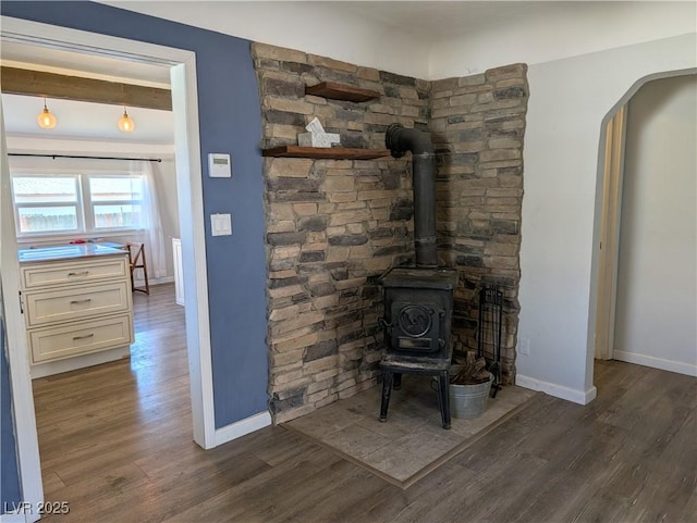 interior details with arched walkways, wood finished floors, a wood stove, and baseboards