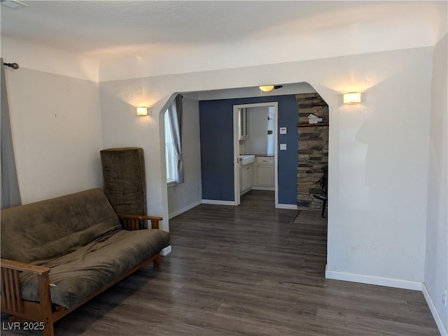 living area with arched walkways, dark wood-style flooring, and baseboards