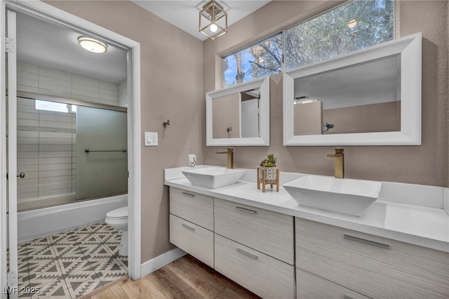 full bathroom with double vanity, shower / bath combination with glass door, a sink, and toilet