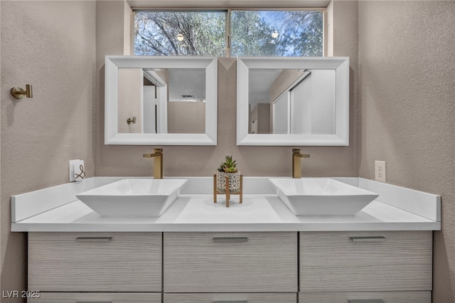 full bathroom with a textured wall, double vanity, and a sink