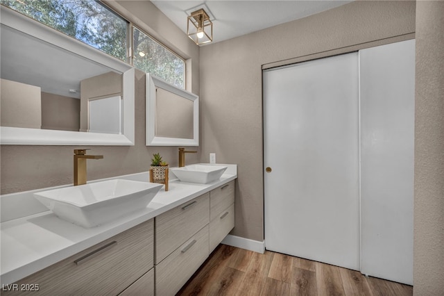 bathroom with a textured wall, double vanity, a sink, and wood finished floors