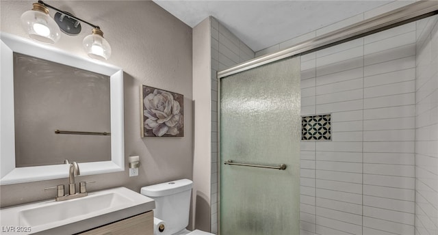 bathroom with a textured wall, tiled shower, vanity, and toilet