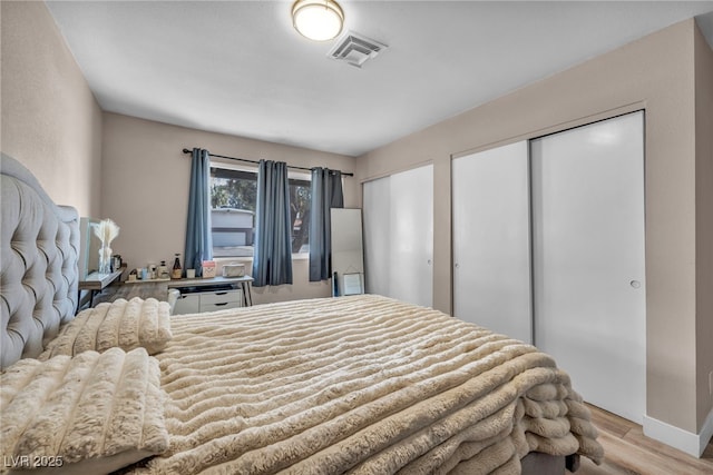 bedroom with wood finished floors, visible vents, and multiple closets