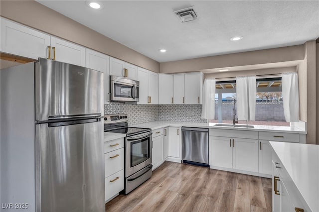 kitchen featuring stainless steel appliances, a sink, visible vents, white cabinets, and light countertops