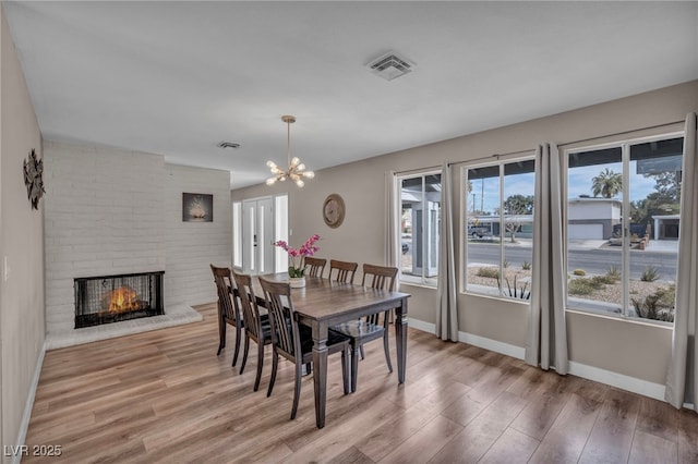 dining area with baseboards, visible vents, wood finished floors, a brick fireplace, and a chandelier